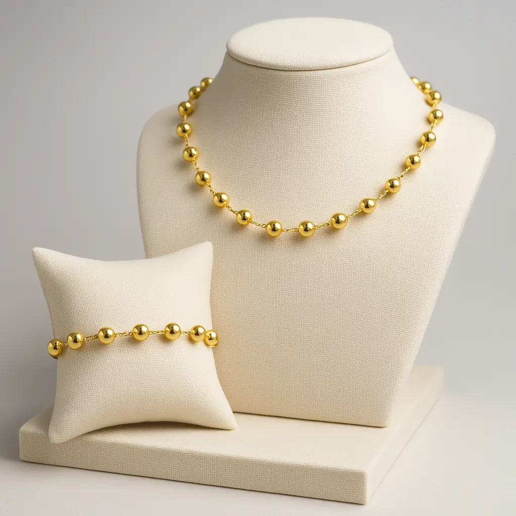 Conjunto de colar e pulseira dourados expostos em suportes claros da JMA Bijoux